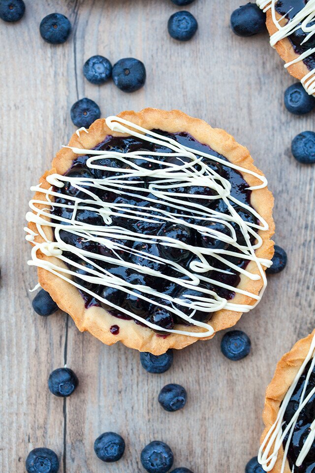 Buttery, crunchy tart shells filled with gooey, fresh blueberry filling and a white chocolate drizzle! | spachethespatula.com #recipe