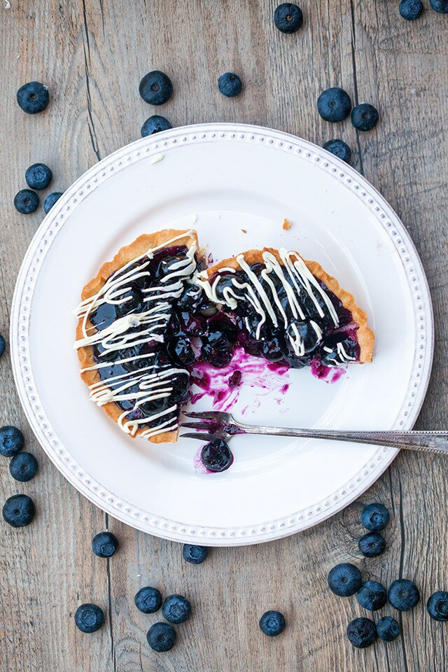 Buttery, crunchy tart shells filled with gooey, fresh blueberry filling and a white chocolate drizzle! | spachethespatula.com #recipe